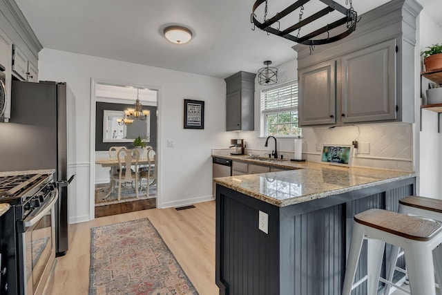 kitchen with sink, gray cabinetry, stainless steel gas range, and kitchen peninsula