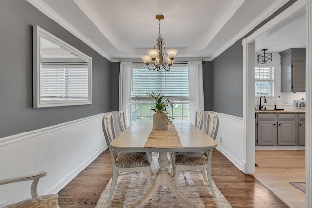 dining area featuring hardwood / wood-style flooring, ornamental molding, a raised ceiling, and a notable chandelier