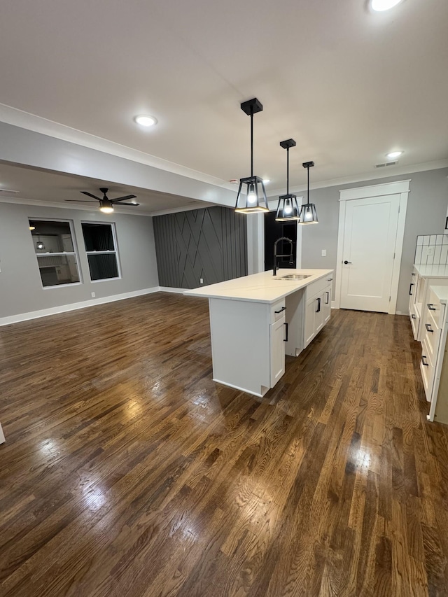 kitchen featuring pendant lighting, sink, crown molding, white cabinetry, and an island with sink