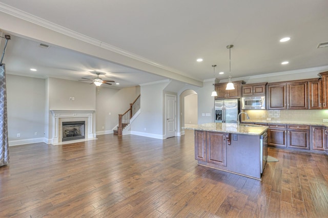 kitchen with pendant lighting, a kitchen island with sink, stainless steel appliances, tasteful backsplash, and light stone countertops