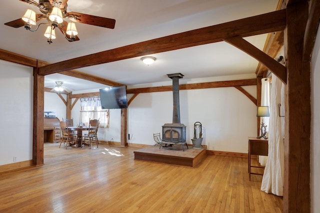 living area with a wood stove, baseboards, beam ceiling, and wood finished floors