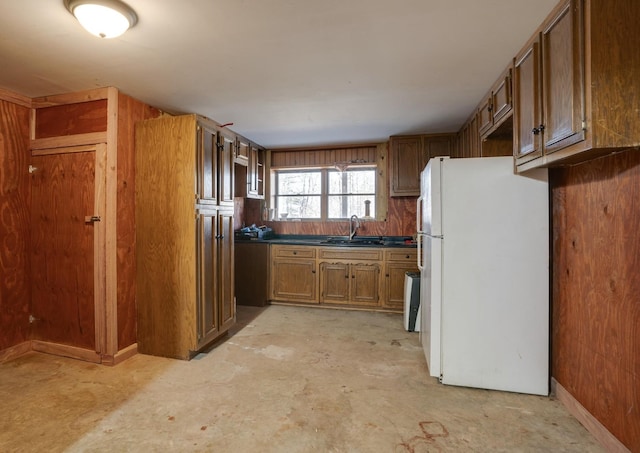 kitchen featuring unfinished concrete floors, freestanding refrigerator, dark countertops, brown cabinets, and a sink