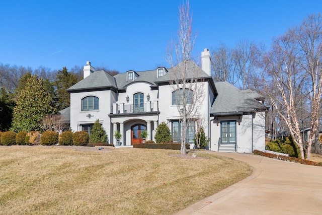 french country home featuring a balcony, a front lawn, and french doors