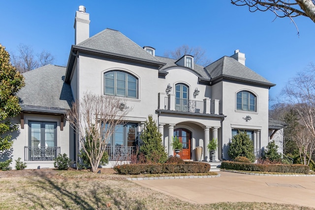 french country home with french doors, a balcony, and a front lawn