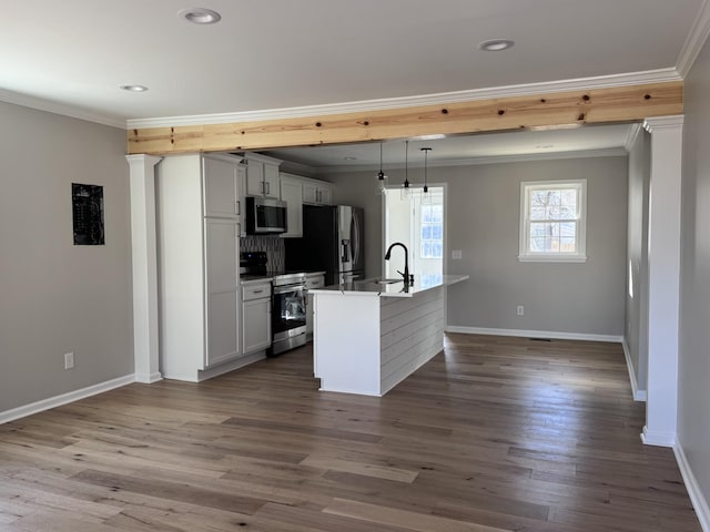 kitchen featuring crown molding, appliances with stainless steel finishes, a center island with sink, and decorative light fixtures