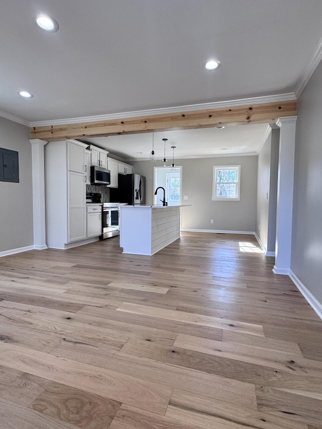 interior space with hanging light fixtures, appliances with stainless steel finishes, electric panel, a kitchen island with sink, and white cabinets