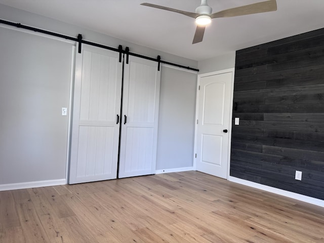 unfurnished bedroom featuring light hardwood / wood-style floors, a barn door, ceiling fan, and wood walls