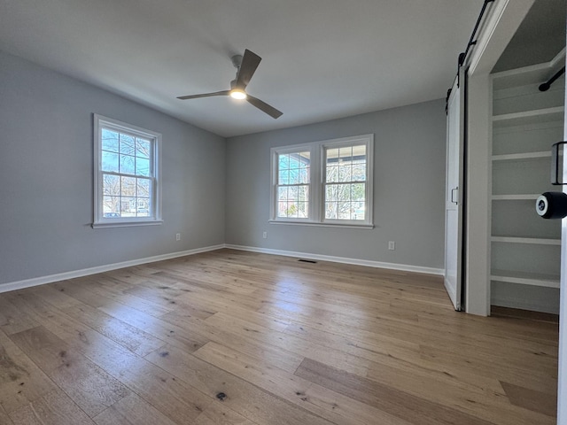 spare room featuring ceiling fan, a barn door, and light wood-type flooring