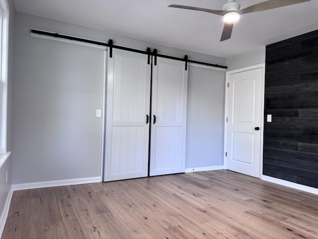 unfurnished bedroom featuring a closet, a barn door, ceiling fan, and light wood-type flooring