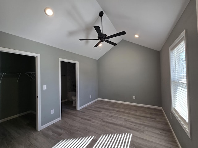 unfurnished bedroom featuring hardwood / wood-style flooring, connected bathroom, a spacious closet, vaulted ceiling, and a closet