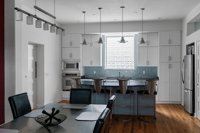 kitchen featuring backsplash, decorative light fixtures, stainless steel appliances, and white cabinets