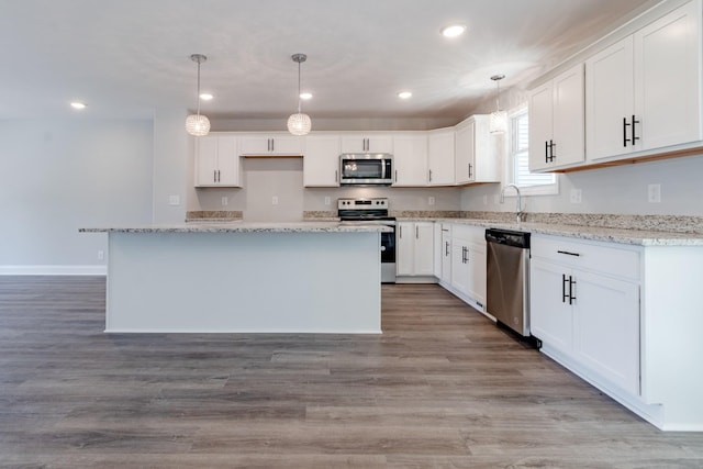 kitchen with white cabinets, hanging light fixtures, a center island, light hardwood / wood-style floors, and stainless steel appliances