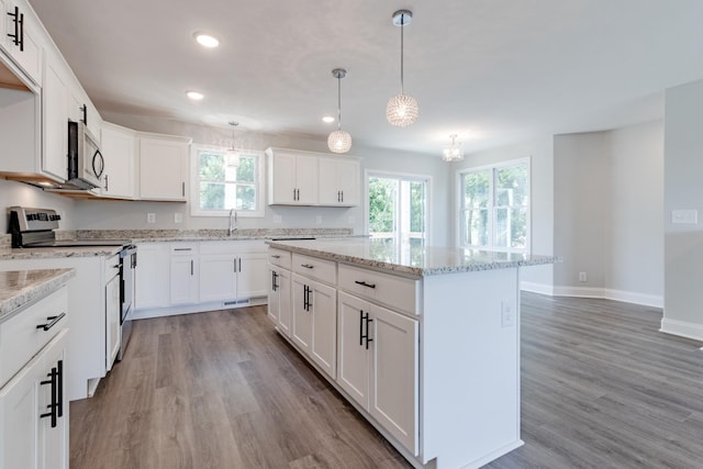 kitchen featuring pendant lighting, appliances with stainless steel finishes, white cabinetry, a center island, and light wood-type flooring