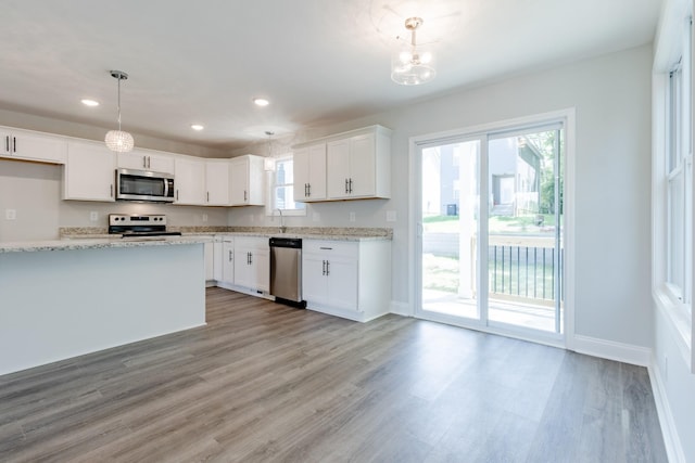 kitchen featuring light stone counters, hanging light fixtures, white cabinets, and appliances with stainless steel finishes