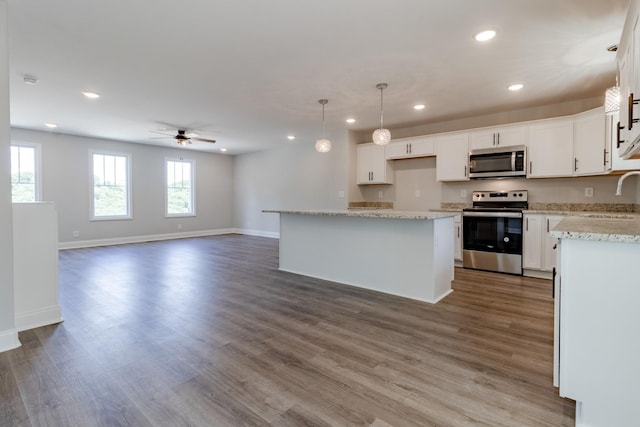 kitchen with pendant lighting, white cabinetry, hardwood / wood-style floors, stainless steel appliances, and a kitchen island