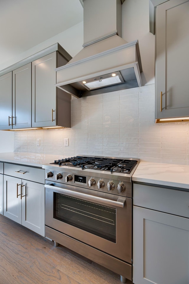 kitchen with premium range hood, gas range, light stone counters, gray cabinets, and backsplash