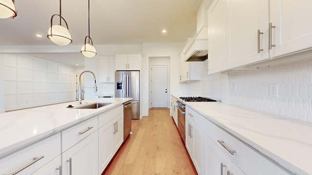 kitchen featuring sink, white cabinetry, light stone counters, decorative light fixtures, and appliances with stainless steel finishes