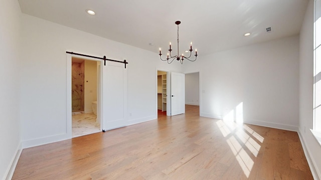 empty room featuring an inviting chandelier, a barn door, and light wood-type flooring