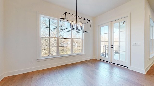 unfurnished dining area with wood-type flooring, french doors, and a chandelier