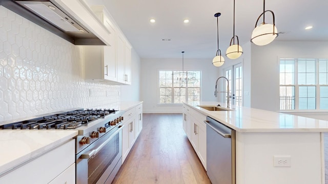 kitchen with appliances with stainless steel finishes, decorative light fixtures, sink, a kitchen island with sink, and custom range hood