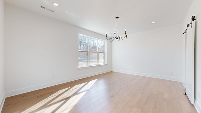 empty room with a notable chandelier, a barn door, and light wood-type flooring