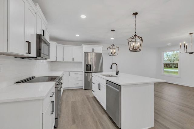 kitchen featuring sink, appliances with stainless steel finishes, a kitchen island with sink, hanging light fixtures, and white cabinetry