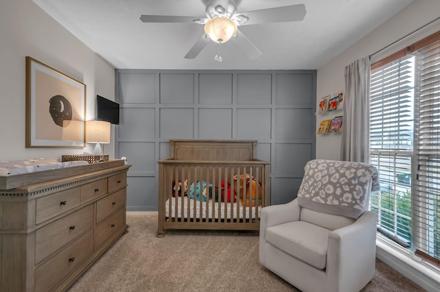 bedroom with light colored carpet, a decorative wall, a crib, and multiple windows