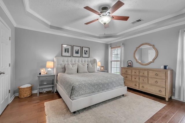 bedroom featuring visible vents, a raised ceiling, wood finished floors, crown molding, and a textured ceiling