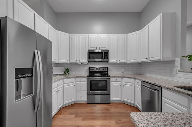 kitchen with appliances with stainless steel finishes, white cabinetry, light stone counters, and light wood finished floors