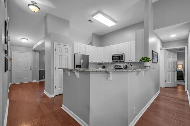 kitchen featuring visible vents, white cabinets, appliances with stainless steel finishes, a breakfast bar area, and a peninsula