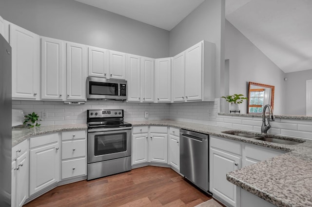 kitchen with decorative backsplash, appliances with stainless steel finishes, wood finished floors, white cabinetry, and a sink