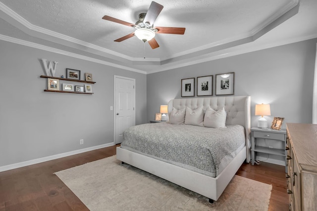 bedroom featuring a tray ceiling, dark wood finished floors, ornamental molding, a textured ceiling, and baseboards