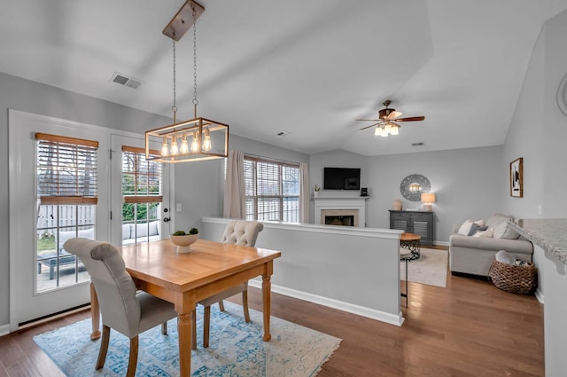 dining room featuring a fireplace, wood finished floors, visible vents, a ceiling fan, and vaulted ceiling