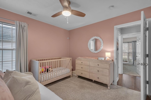 bedroom with light carpet, a nursery area, visible vents, and a ceiling fan