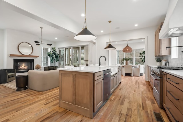 kitchen with hanging light fixtures, light hardwood / wood-style flooring, an island with sink, custom range hood, and stainless steel appliances