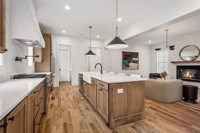 kitchen featuring sink, appliances with stainless steel finishes, hanging light fixtures, a center island with sink, and custom exhaust hood