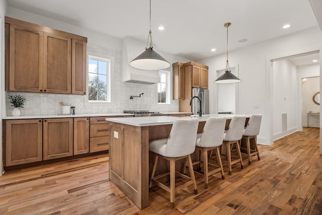 kitchen with decorative light fixtures, light hardwood / wood-style floors, an island with sink, and backsplash