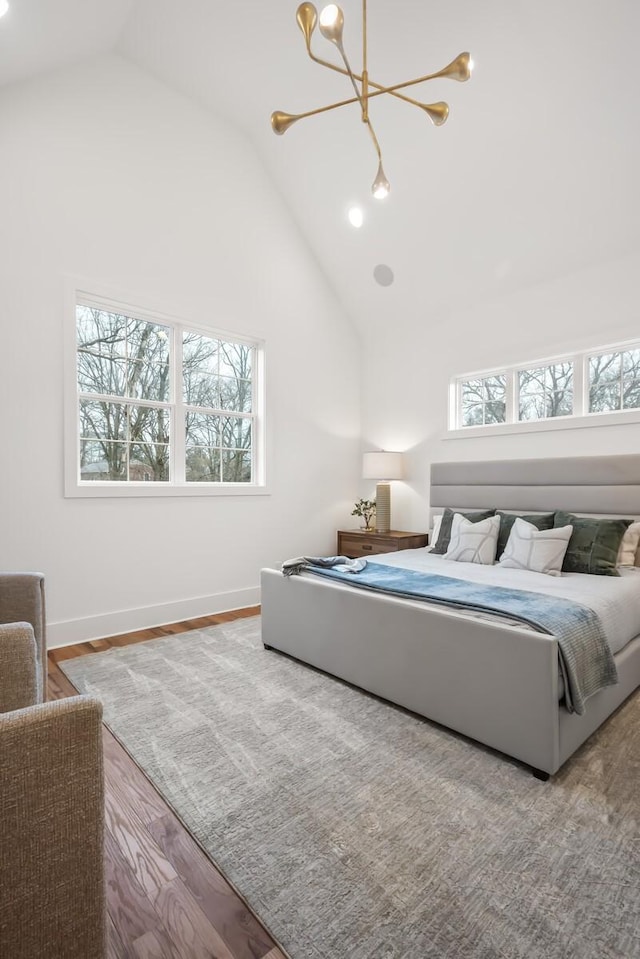 bedroom featuring multiple windows, wood-type flooring, a notable chandelier, and high vaulted ceiling