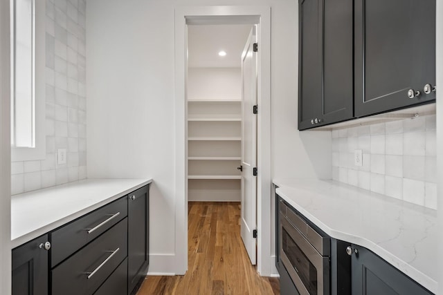 bar featuring tasteful backsplash, light stone countertops, stainless steel microwave, and light hardwood / wood-style flooring