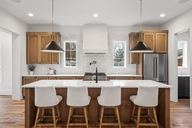 kitchen with decorative backsplash, wall chimney exhaust hood, high end fridge, and a center island with sink