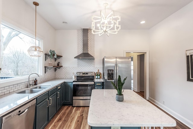 kitchen featuring wall chimney range hood, sink, appliances with stainless steel finishes, tasteful backsplash, and decorative light fixtures