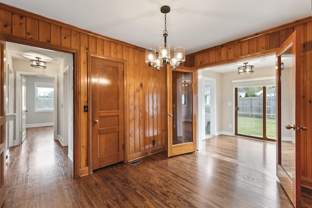 unfurnished dining area with dark wood-type flooring, wooden walls, and a notable chandelier