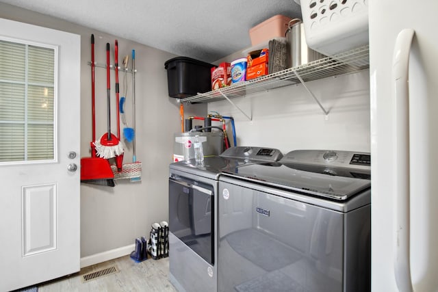 clothes washing area with independent washer and dryer, a textured ceiling, water heater, and light hardwood / wood-style flooring