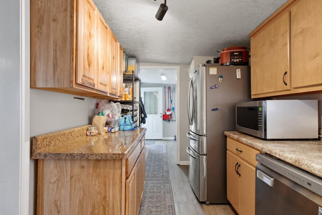 kitchen featuring stainless steel appliances, light stone countertops, light hardwood / wood-style floors, a textured ceiling, and light brown cabinets