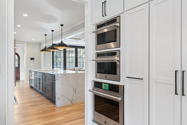 kitchen featuring light stone counters, light hardwood / wood-style flooring, hanging light fixtures, ornamental molding, and white cabinets