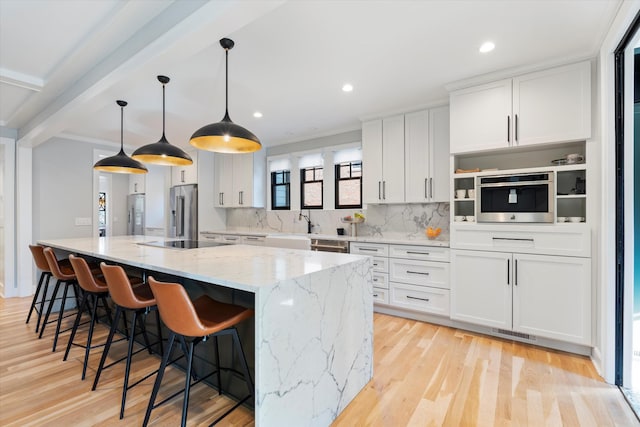 kitchen with a large island, white cabinetry, hanging light fixtures, stainless steel appliances, and light stone counters