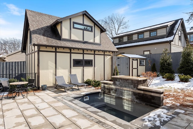 snow covered back of property featuring a patio and a storage unit