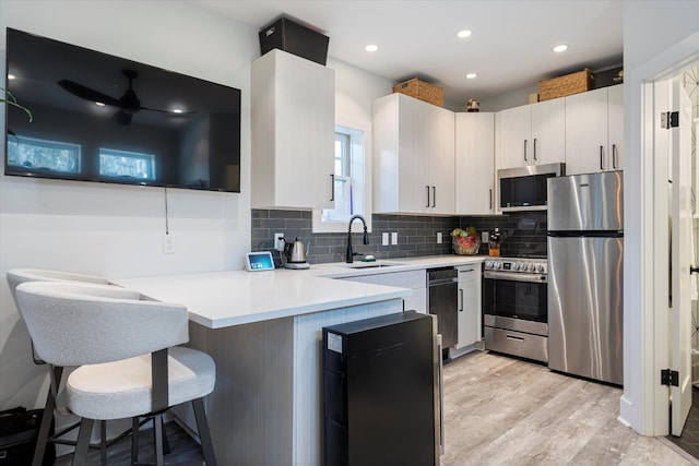 kitchen with tasteful backsplash, a kitchen bar, light hardwood / wood-style floors, kitchen peninsula, and stainless steel appliances