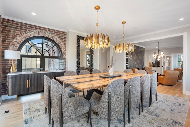 dining space featuring an inviting chandelier, brick wall, crown molding, and light hardwood / wood-style floors