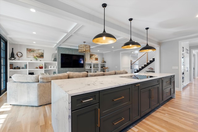 kitchen with hanging light fixtures, coffered ceiling, a kitchen island with sink, light hardwood / wood-style floors, and light stone countertops